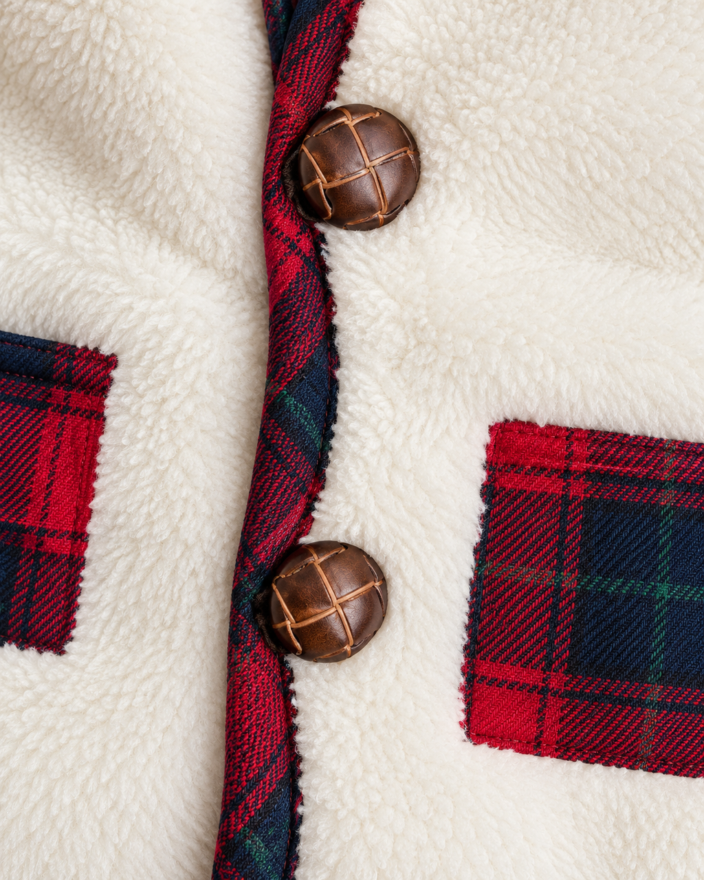 Close-up of a white sherpa fleece jacket with red and navy tartan plaid trim, brown buttons, and matching plaid pocket details.