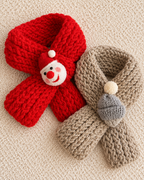 Two chunky knit winter scarves laid flat on a cream textured background. One scarf is bright red with a small snowman face decoration wearing a red hat.